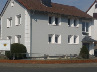 Modernisiertes Wohnhaus mit hellgrauem Fassadenanstrich, weiß abgesetzten Fensterrahmen und strukturierter Oberfläche – elegante und gepflegte Außenansicht.