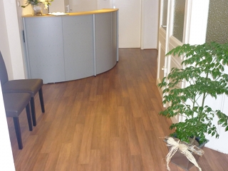 Moderner Empfangsbereich mit PVC-Boden in Holzoptik, grauer Empfangstheke und grüner Pflanze. Der Boden schafft eine warme und einladende Atmosphäre.