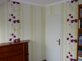 Hell gestaltetes Zimmer mit floral gemusterter Tapete in Grün- und Violetttönen – professionell tapezierte Wand für ein freundliches Raumambiente.