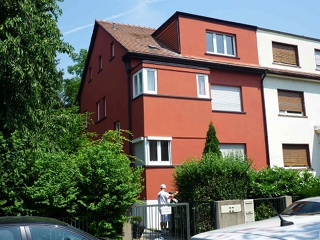Mehrfamilienhaus mit frisch gestrichener roter Fassade und weißen Fensterrahmen – moderner, kontrastreicher Außenanstrich bei sonnigem Wetter.