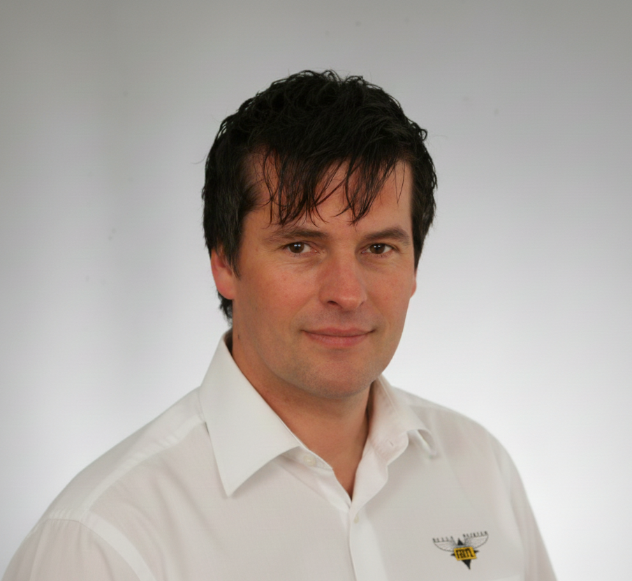 Porträt eines freundlichen Handwerkers im weißen Arbeitshemd vor neutralem Hintergrund.